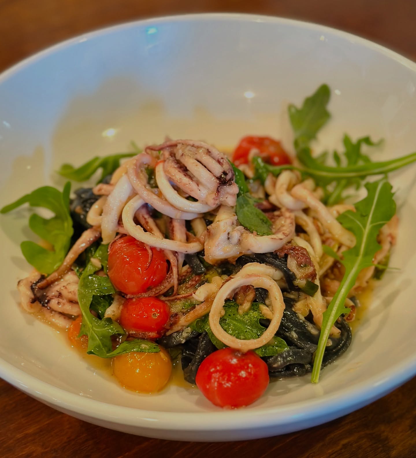 Squid ink pasta with calamari and cherry tomatoes, on the Trattoria's dark wood table