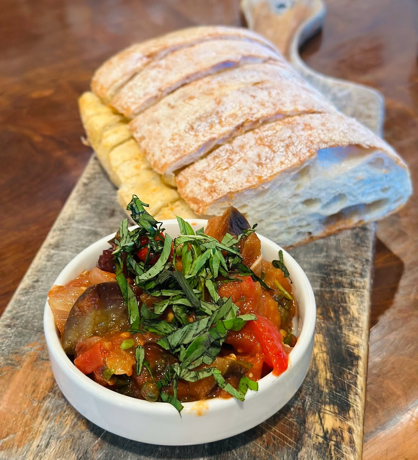 A loaf of the Trattoria's rustic ciabatta, sliced on a board beside a bowl of bruschetta topping