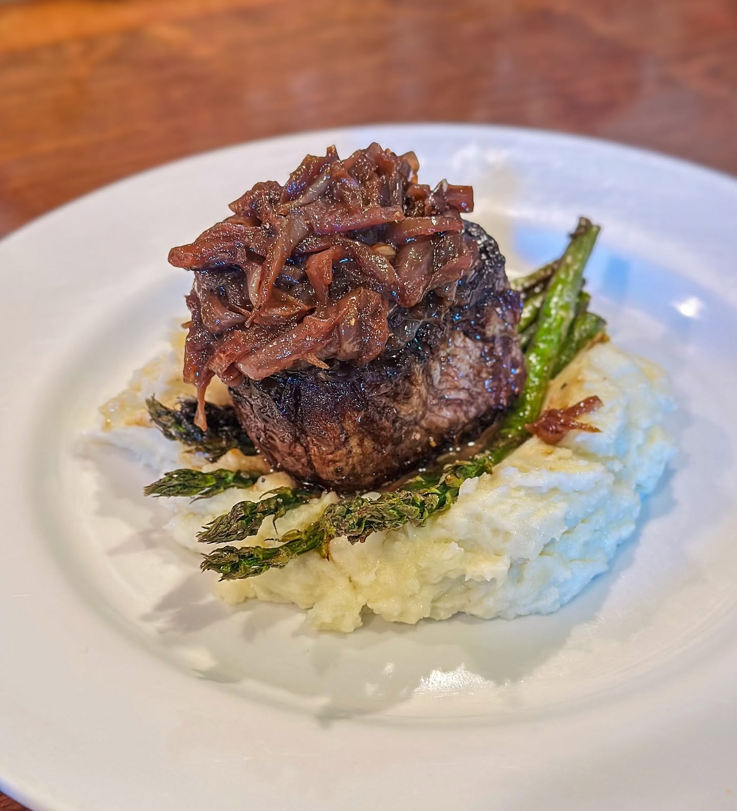 Filet with caramelized onions over mashed potatoes and asparagus, on the Trattoria's dark wood table