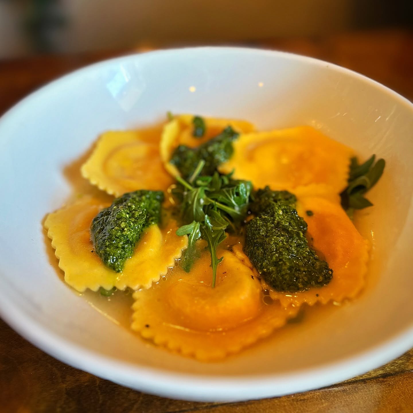 Golden ravioli with pesto and arugula, on the Trattoria's dark wood table
