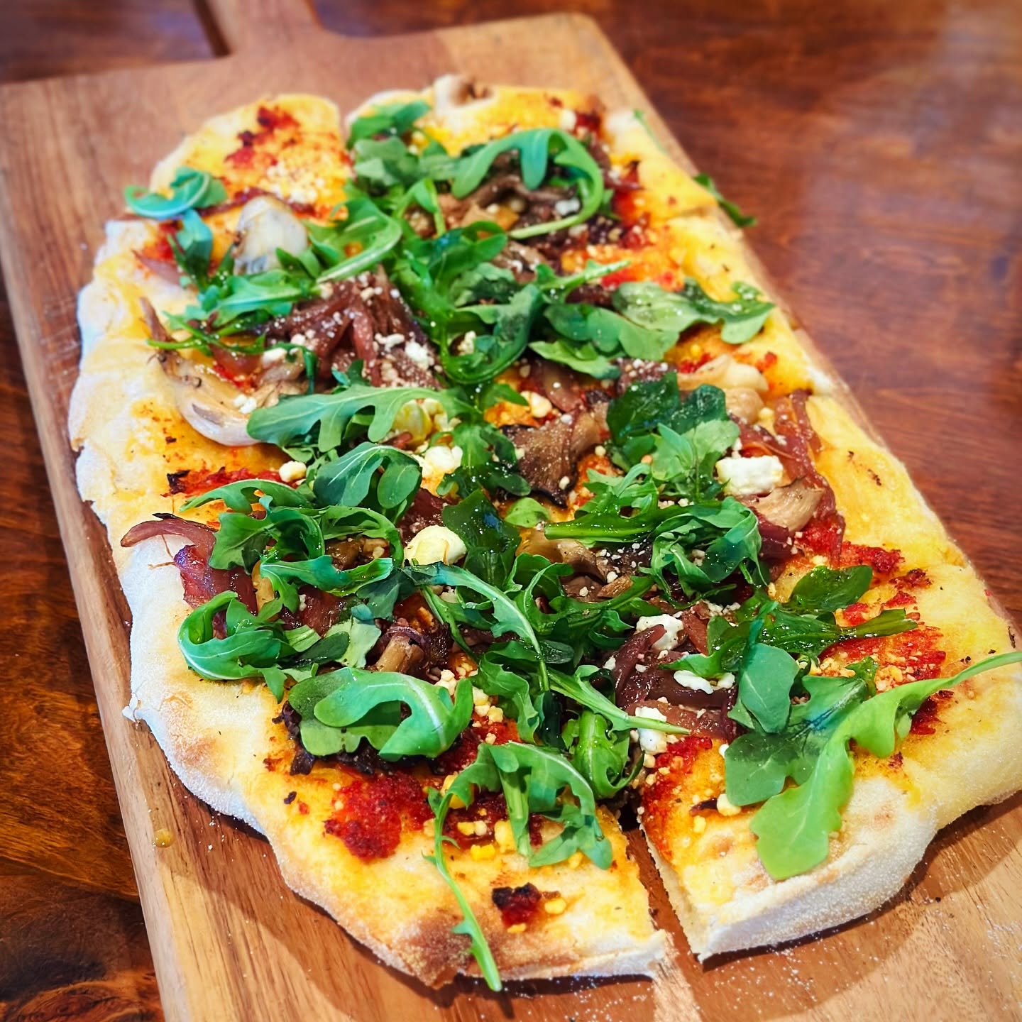 Flatbread with arugula on a wooden board, on the Trattoria's dark wood table