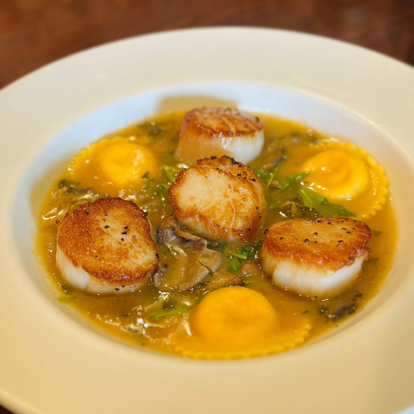 Seared scallops with ravioli in a saffron broth, on the Trattoria's dark wood table