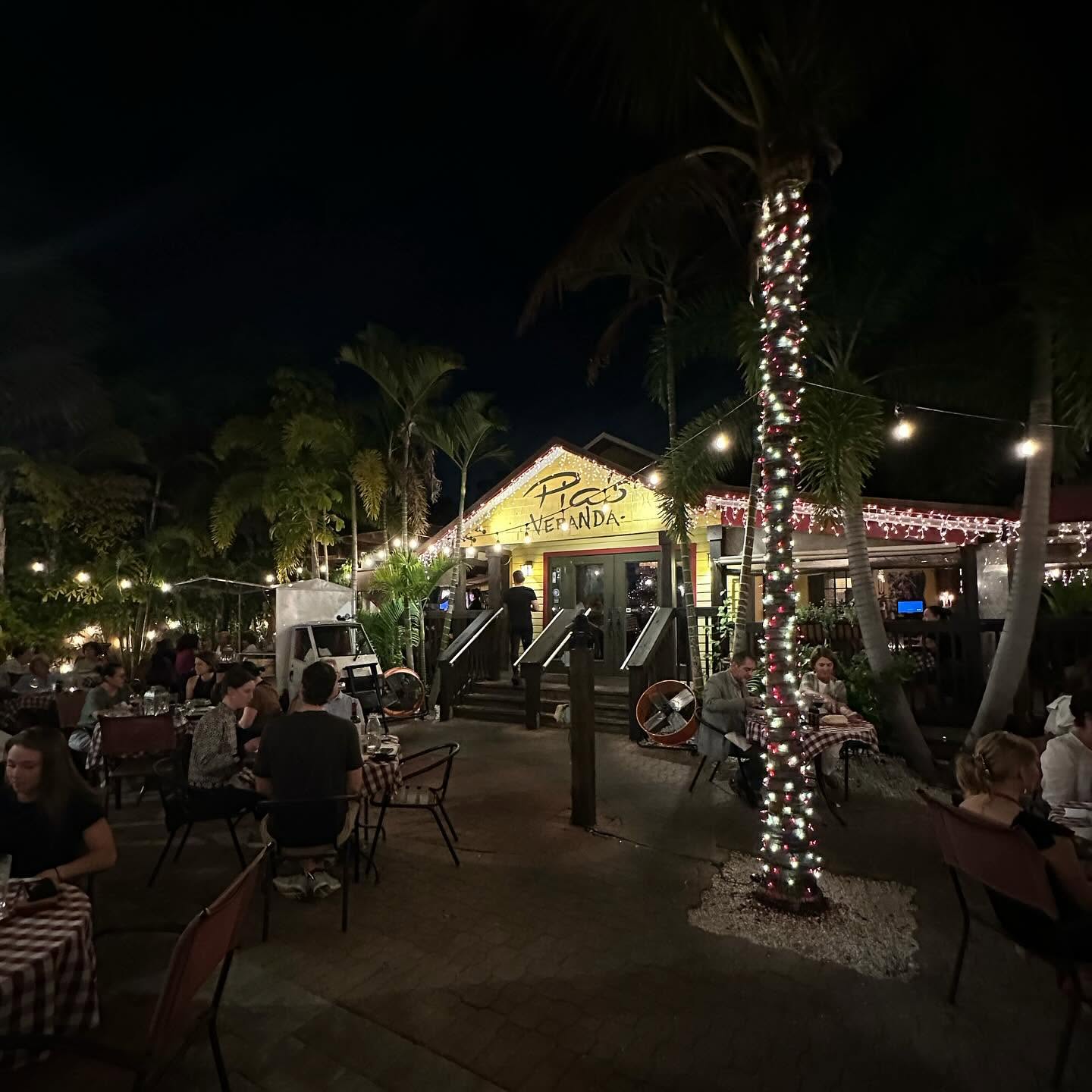 Guests dining in the Veranda's garden at night under string lights and a lit palm