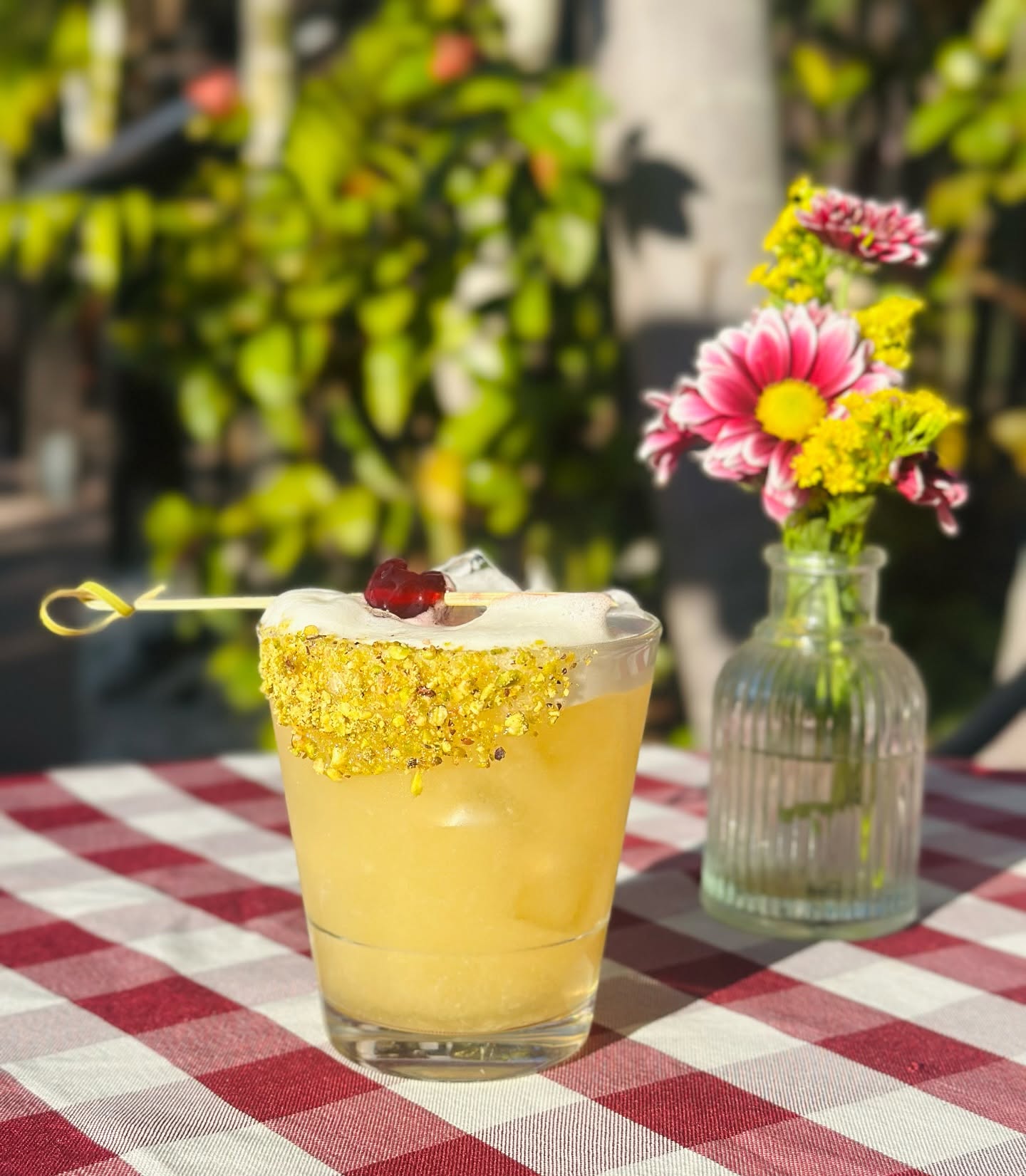 A gold-rimmed cocktail beside a jar of flowers on a gingham table