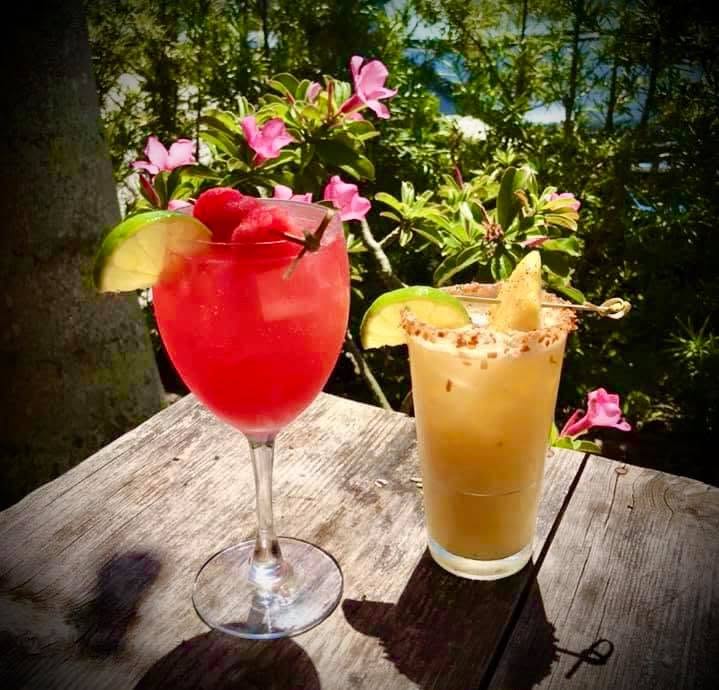 A red cocktail and a sugared-rim drink on a weathered table among flowers