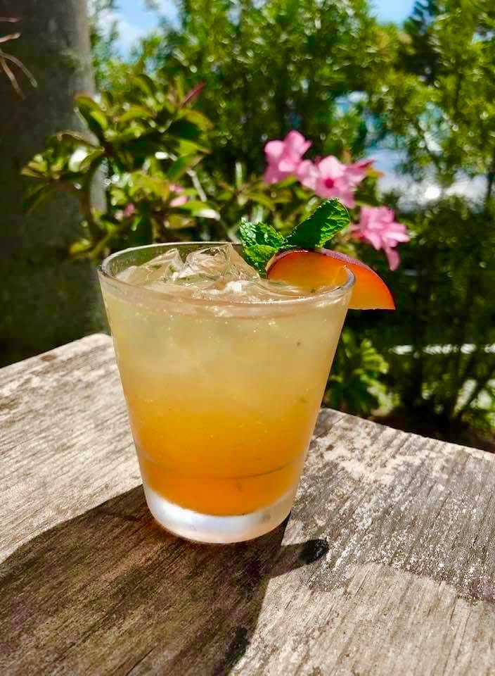 An amber cocktail with a pink flower garnish on a garden table