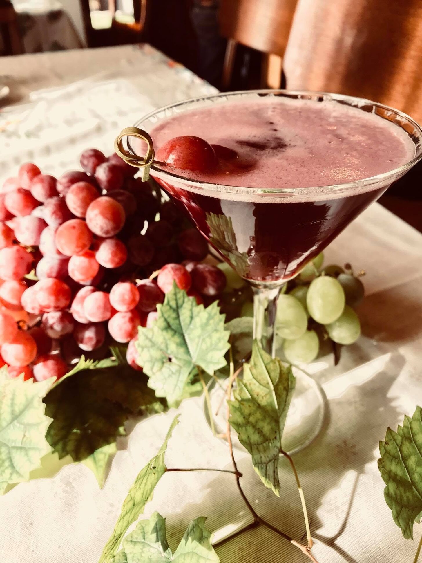 A red cocktail beside a bunch of grapes and vine leaves