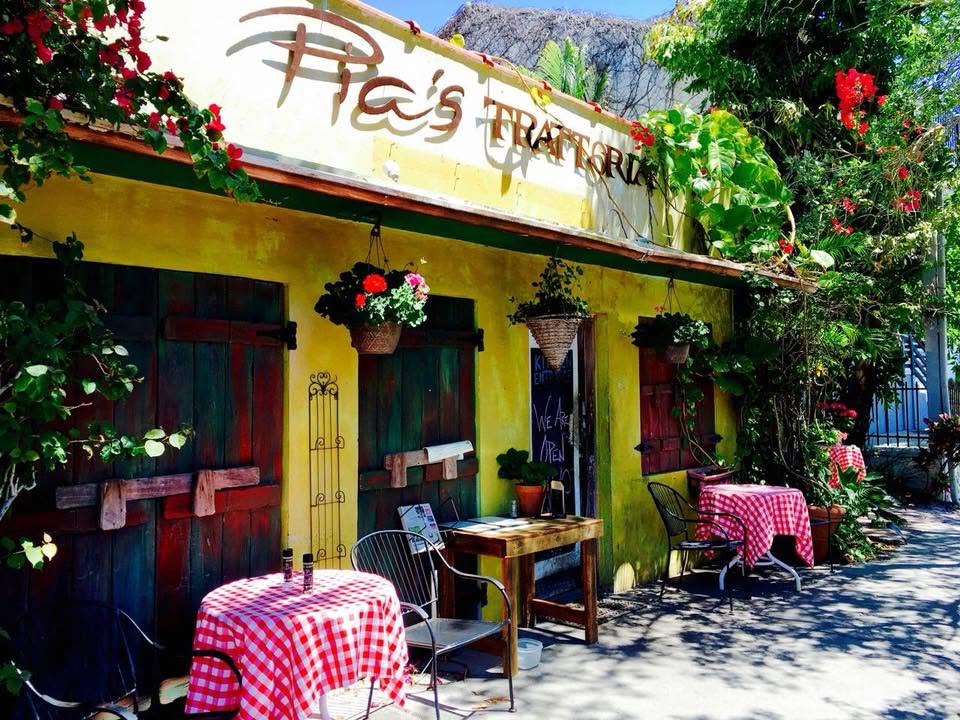 The Trattoria's yellow stucco front with dark green shutters and gingham tables on the sidewalk
