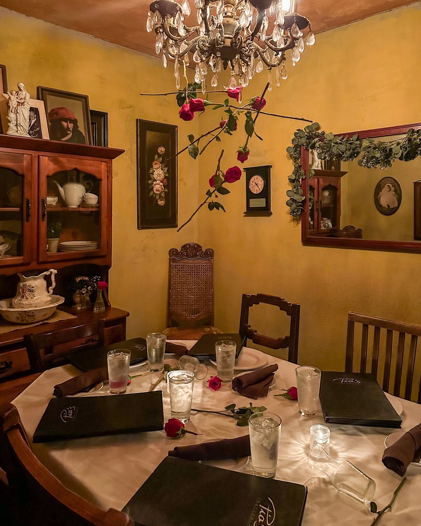 A round table under a chandelier, roses strung over the china cabinet at Pia's Trattoria