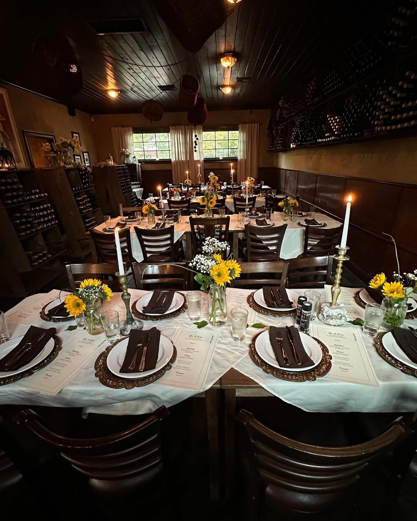 A dinner table set with sunflowers and tall candles in the Trattoria's wine-rack room