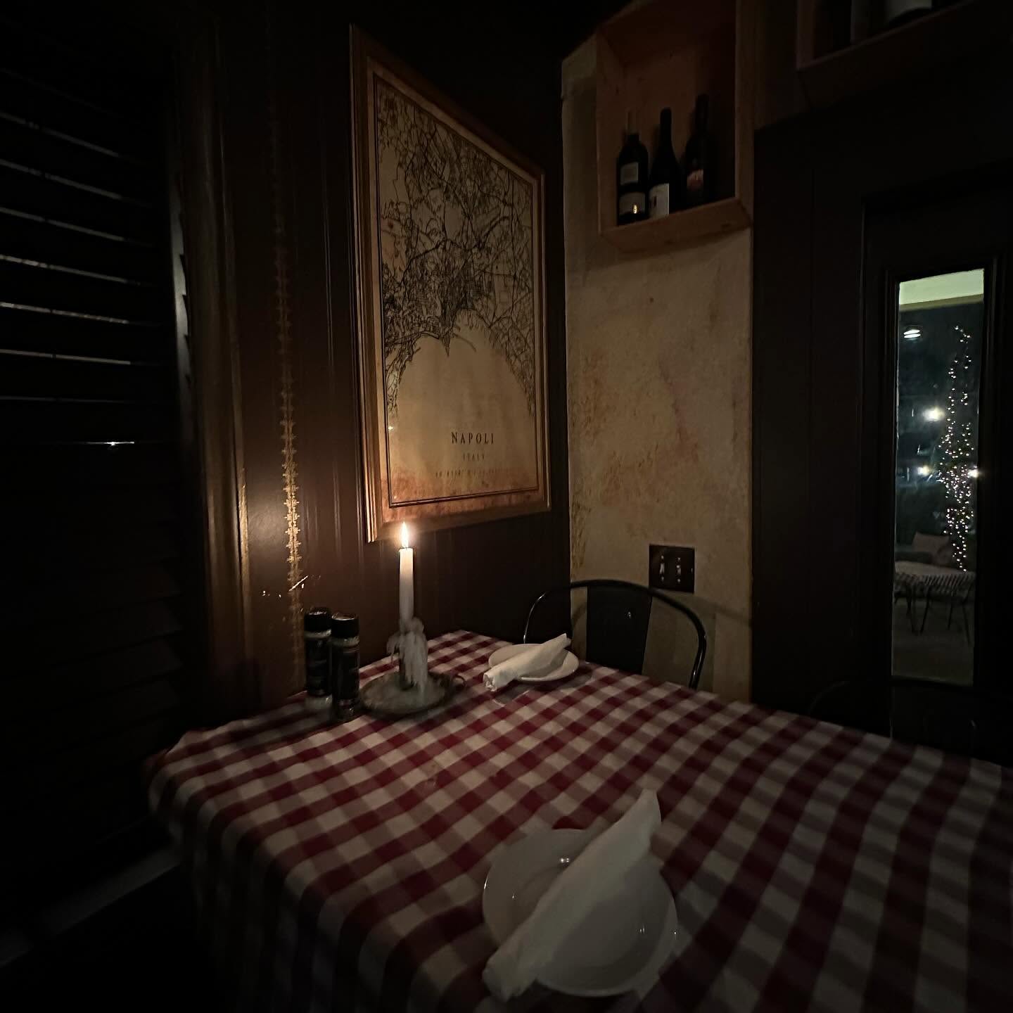 A single candle on a red gingham table in a dark corner of the Trattoria