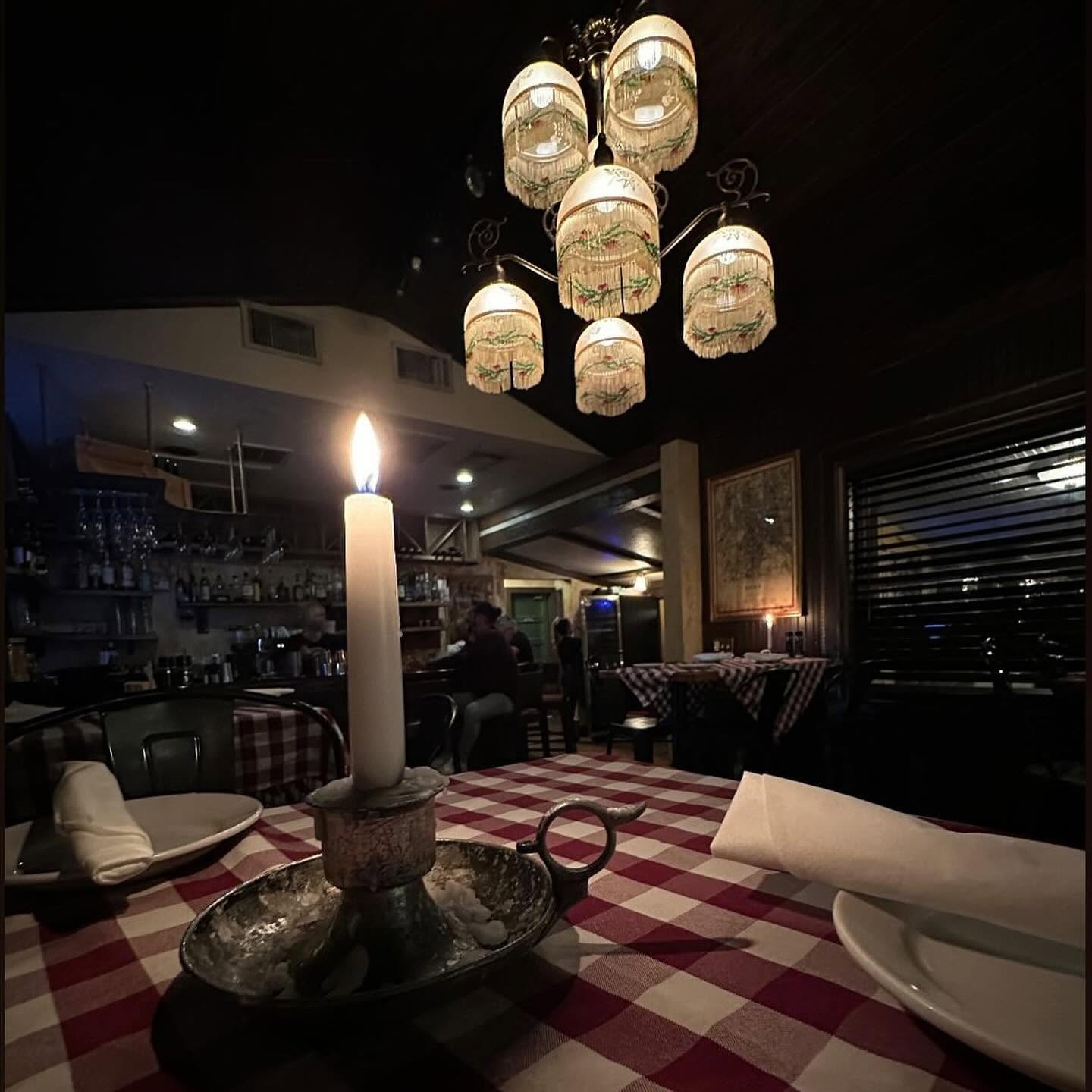 A candle burning on a red-and-white checked tablecloth under a crystal chandelier in Pia's Trattoria