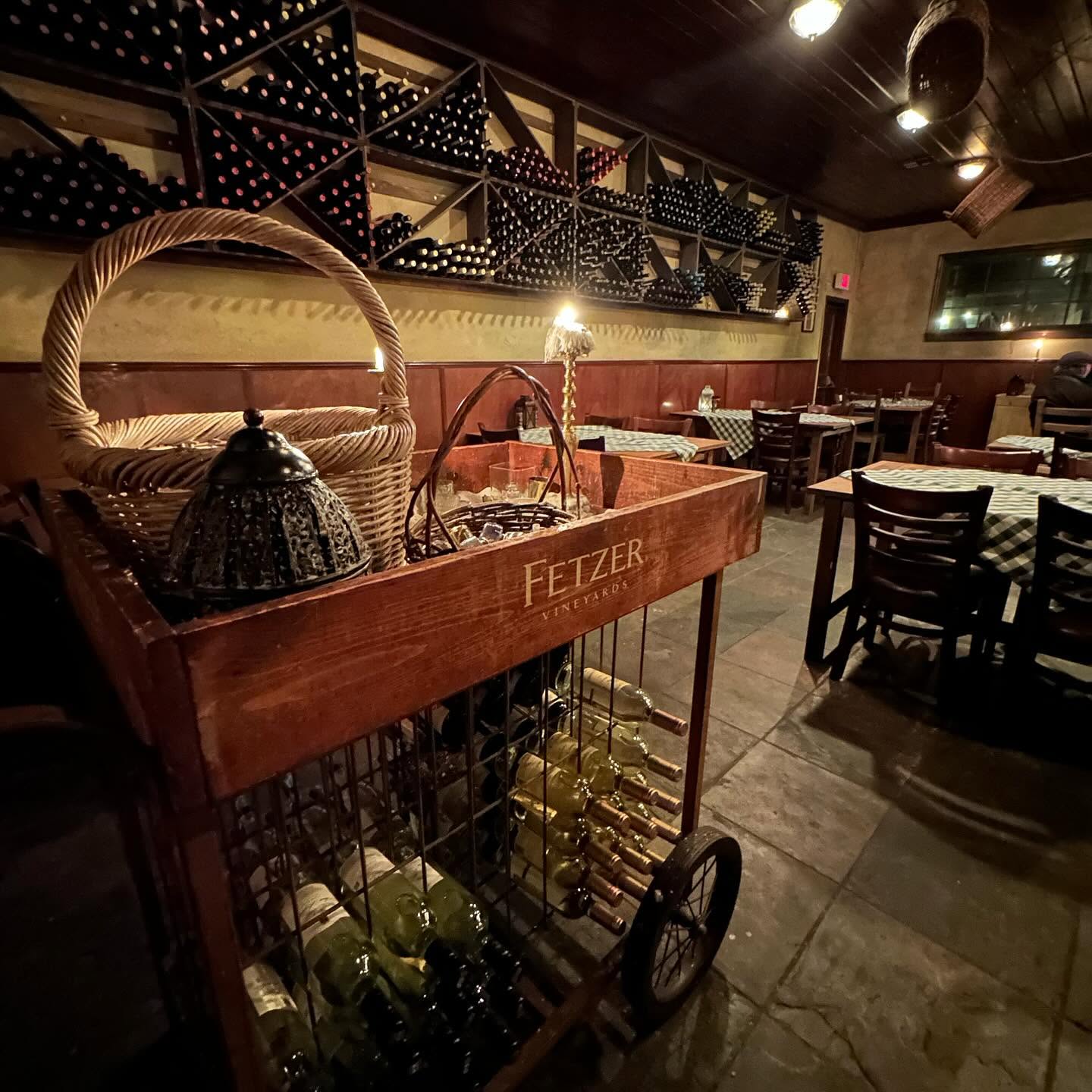 A wooden wine cart and floor-to-ceiling wine racks inside the Trattoria