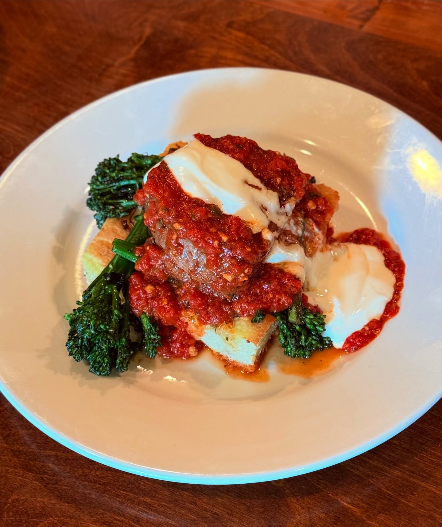 Meatball with burrata, tomato sauce and broccolini, on the Trattoria's dark wood table