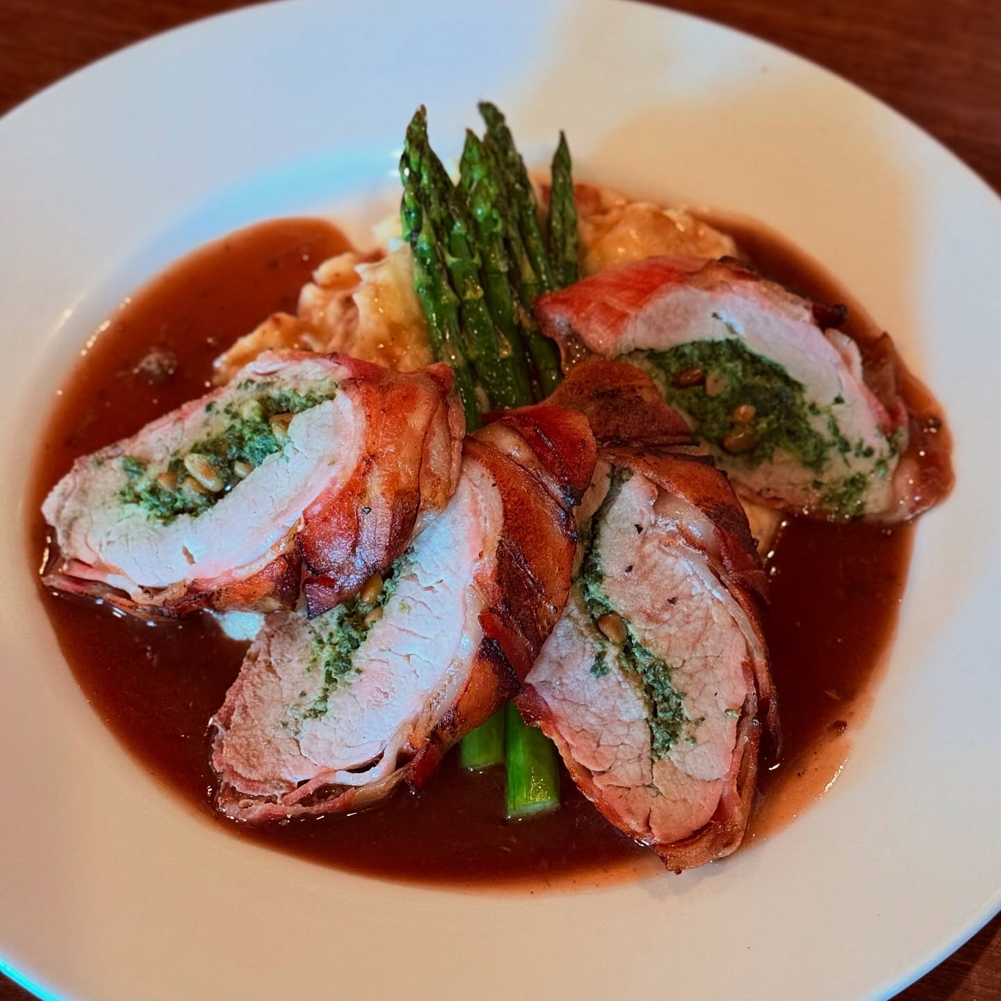 Sliced stuffed pork tenderloin with asparagus in a wine reduction, on the Trattoria's dark wood table